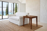 Polcenigo side table in Dark Burl at the arm of a white slipcovered sofa in a cliff-top villa, with a travertine wall