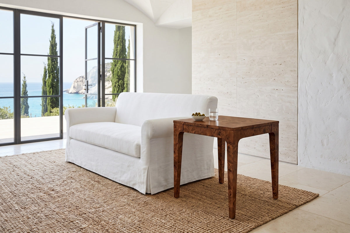 Polcenigo side table in Dark Burl at the arm of a white slipcovered sofa in a cliff-top villa, with a travertine wall