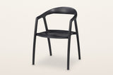 Pollica solid ash dining armchair in Black, three-quarter view on a warm white studio backdrop