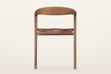Pollica dining chair in Caramel from behind on a warm white studio backdrop: the back is open under the curved band