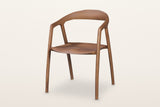 Pollica solid ash dining armchair in Caramel, three-quarter view on a warm white studio backdrop: one curved band runs round