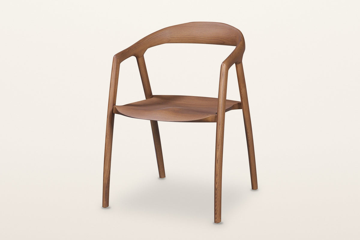 Pollica solid ash dining armchair in Caramel, three-quarter view on a warm white studio backdrop: one curved band runs round