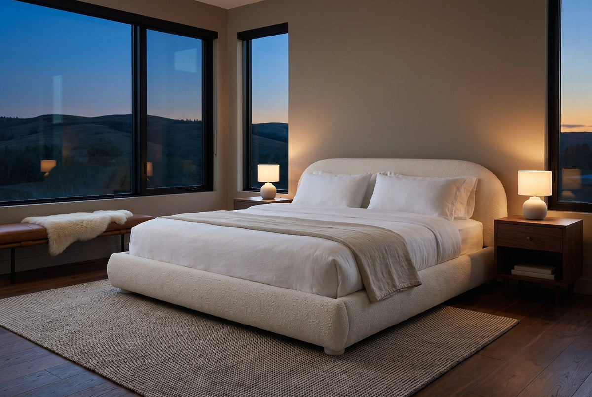Pollutri bed in cream boucle in a bedroom at dusk, two lamps lit, dark foothills through the windows