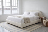 Pollutri bed in cream boucle in a white board-walled bedroom looking onto the harbour