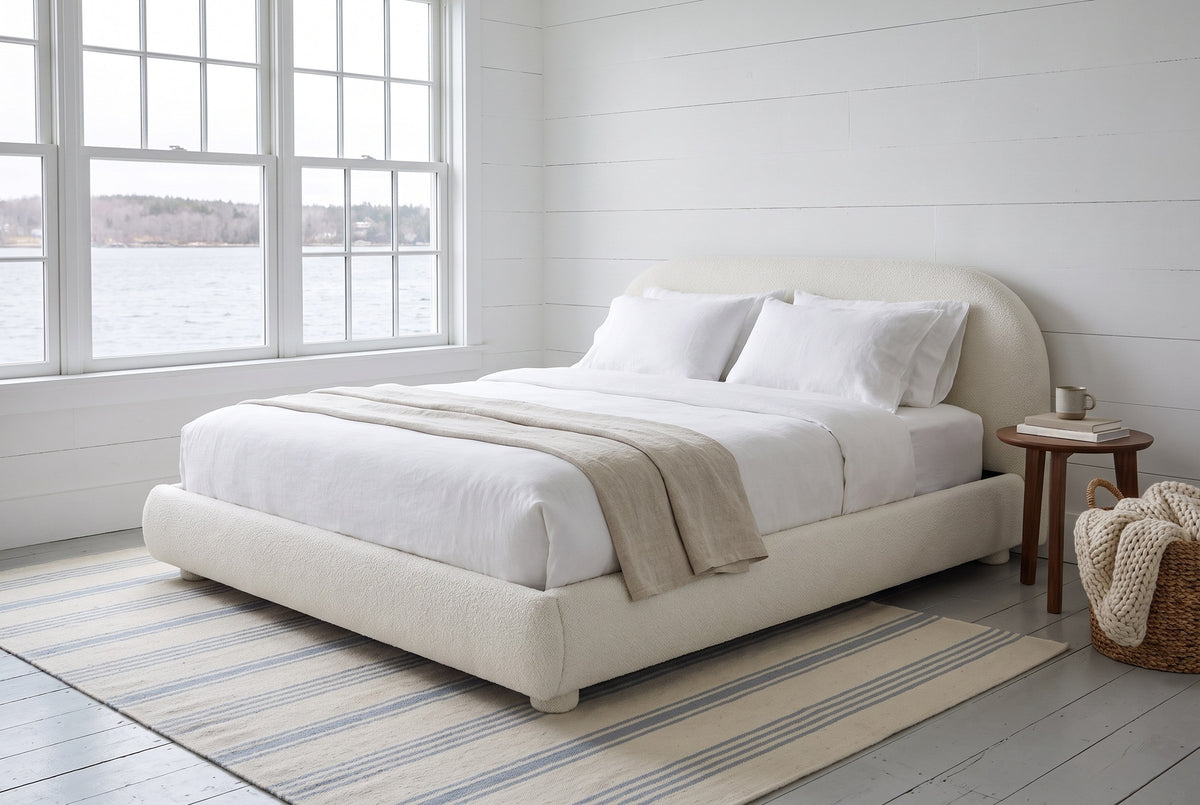 Pollutri bed in cream boucle in a white board-walled bedroom looking onto the harbour