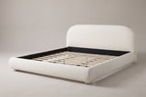 Pollutri upholstered bed in cream white boucle, three-quarter view on a warm grey studio backdrop