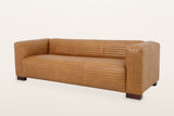 Pontremoli three-seat sofa in Latte top-grain leather with horizontal stitched channels on every face, three-quarter view on a warm white studio backdrop