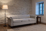 Portovenere sofa against a fieldstone wall in a Quebec City sitting room at dusk, an iron floor lamp lit beside it