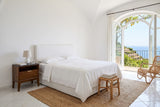 Postignano nightstand beside a white linen bed in a bedroom of an Amalfi cliff villa, under a white barrel vault