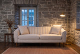 Prato sofa in a stone-walled Quebec City sitting room at dusk, a brass floor lamp lit beside it