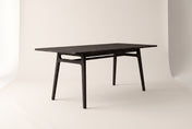 Prescott solid acacia dining table in Antique Black, three-quarter view on a warm off-white studio backdrop