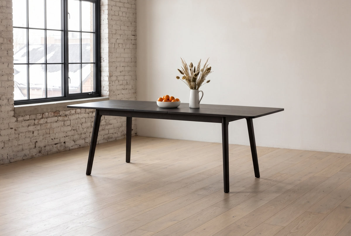Prescott extension dining table in Antique Black opened to 86 in with clementines and dried grasses, in a brick loft in Winnipeg's Exchange District, snowy rooftops outside