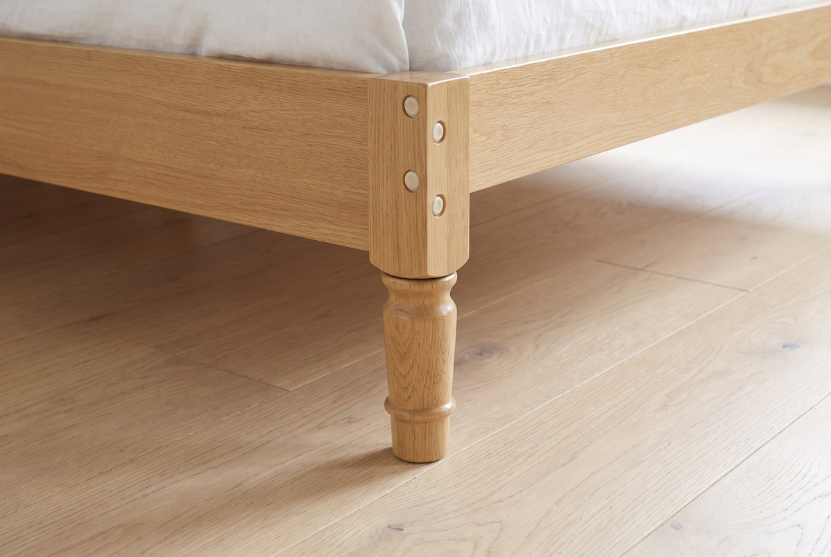 Close-up of a Ravenna foot corner: the corner block with bolt caps and the turned leg on an oak floor