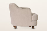 Ripatransone accent chair in Beige from the side on a warm white studio backdrop: the back curving down into the arm