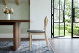 A Rivello dining chair in side profile at a walnut table in an Annapolis Royal garden house