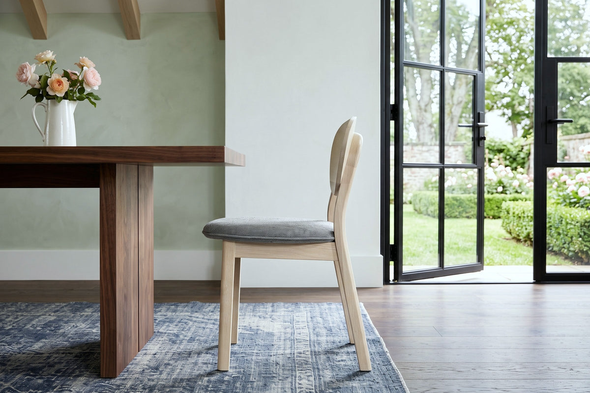 A Rivello dining chair in side profile at a walnut table in an Annapolis Royal garden house