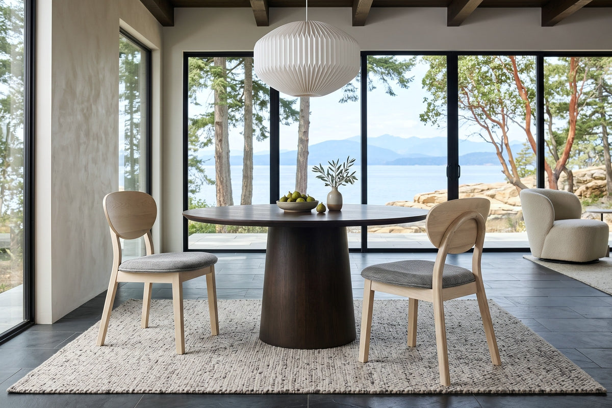 Two Rivello dining chairs in Light Oak at a round espresso-oak pedestal table in a Gabriola Island house, with greige plaster