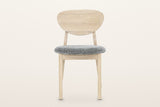 Rivello dining chair in Light Oak, straight front view on a warm white studio backdrop: the pebble back