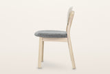 Rivello dining chair in Light Oak, side view on a warm white studio backdrop: the back leans back and the round rear legs rak
