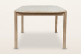 End view of the Rivello dining table in Light Oak on a warm white studio backdrop: the rounded end over round legs