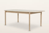 Rivello oak dining table in Light Oak, three-quarter view on a warm white studio backdrop: a long top with rounded ends on fo
