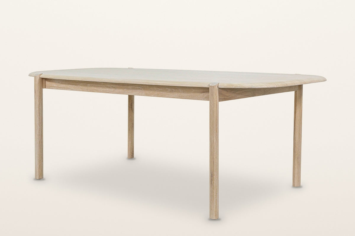 Rivello oak dining table in Light Oak, three-quarter view on a warm white studio backdrop: a long top with rounded ends on fo