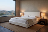 Roccascalegna boucle bed in a plaster bedroom at dusk, two lamps lit, with a picture window onto rolling foothills