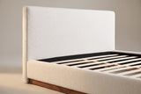 Close-up of the white boucle headboard where the side rail meets it, with the walnut plinth below