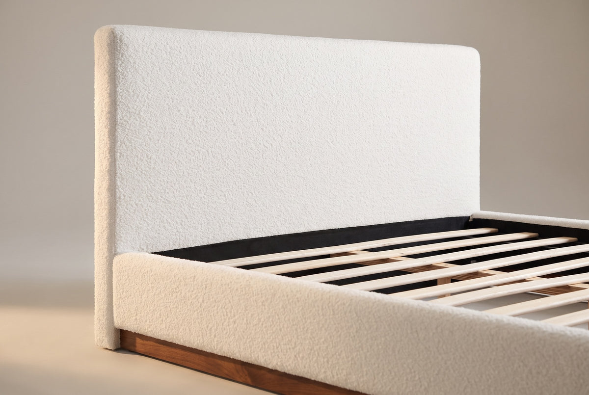 Close-up of the white boucle headboard where the side rail meets it, with the walnut plinth below
