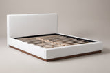 Roccascalegna boucle platform bed in white, three-quarter view on a warm grey studio backdrop, with its walnut plinth