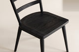 Close-up of one black wire-brushed oak two-slat Rocco dining chair on an off-white backdrop: the sculpted seat and its grain, the lower back slat, the round back posts and the tapered legs