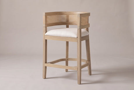Sabaudia cane-back counter stool in Natural Ash, three-quarter view on a warm light-grey studio backdrop