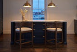 Two Sabaudia counter stools in Walnut in front of a navy kitchen island with a marble counter and a harbour view at blue hour