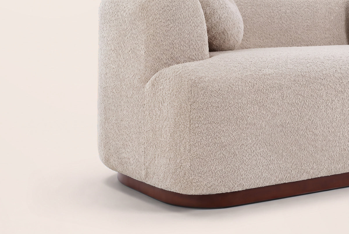 Close-up of the Almond boucle block arm and the walnut-brown rubberwood plinth with its rounded corner
