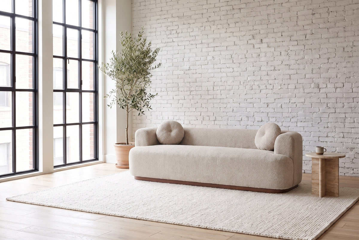 Sabbioneta sofa in Almond boucle against a white brick wall in a bright Montreal loft, an olive tree by the steel windows