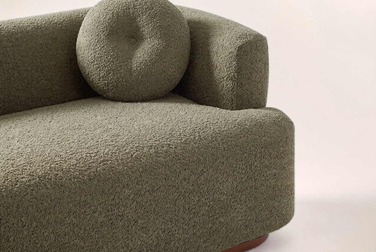 Close-up of the olive green boucle bench seat, a round button pillow and the block arm
