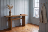 Sanremo console table in antique brown against blue-grey panelling in an entry with a harbour window