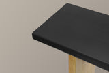 Close-up of the corner of the 2.4-inch black top over a light natural wood leg, fine straight grain under a matte black stain