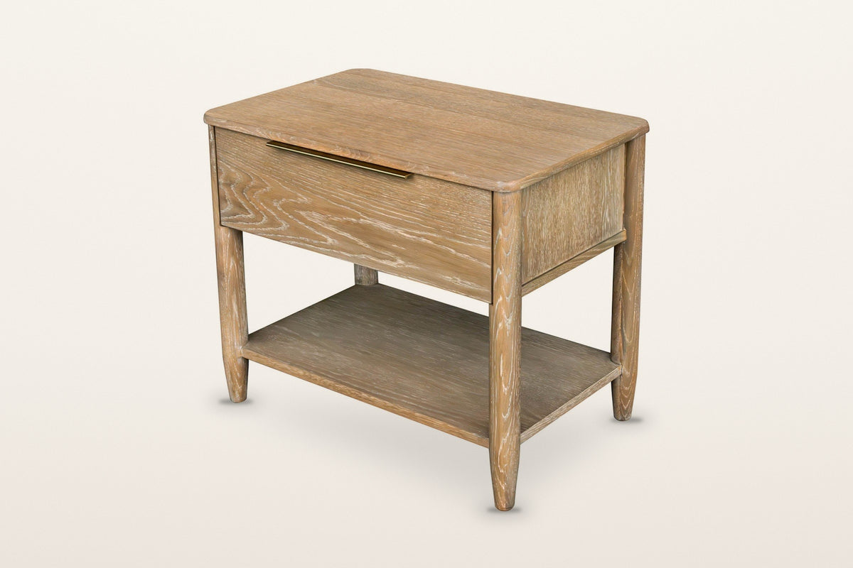 Sarnano nightstand in Sand oak, three-quarter view on a warm white studio backdrop: one wide drawer with a slim brass edge pu