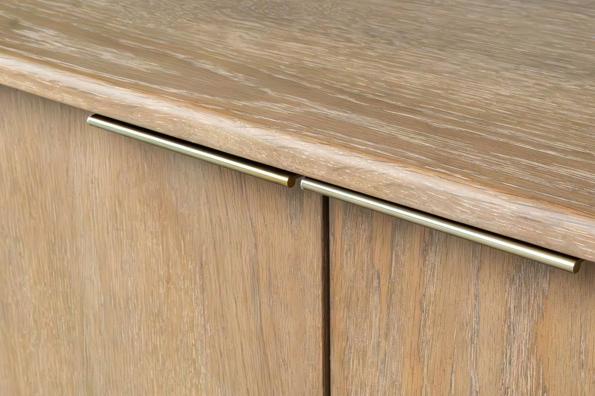 Close-up of two slim brass-finish pulls on the top edge of two Sarnano doors in Sand, below the rounded oak top