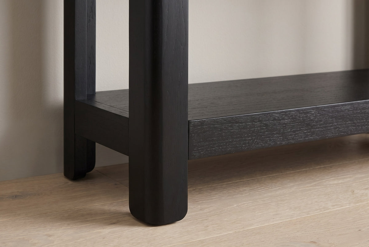 Close-up of a rounded black solid pine leg running past the thick lower shelf into a short rounded foot