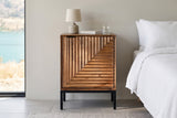 Sarteano nightstand in Pecan mango, front view, beside a white linen bed in a Vernon lakeside bedroom