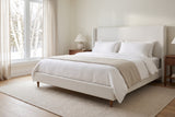 Sarzana wingback bed made up with white linen in a bright bedroom, snow and birch trees outside the window