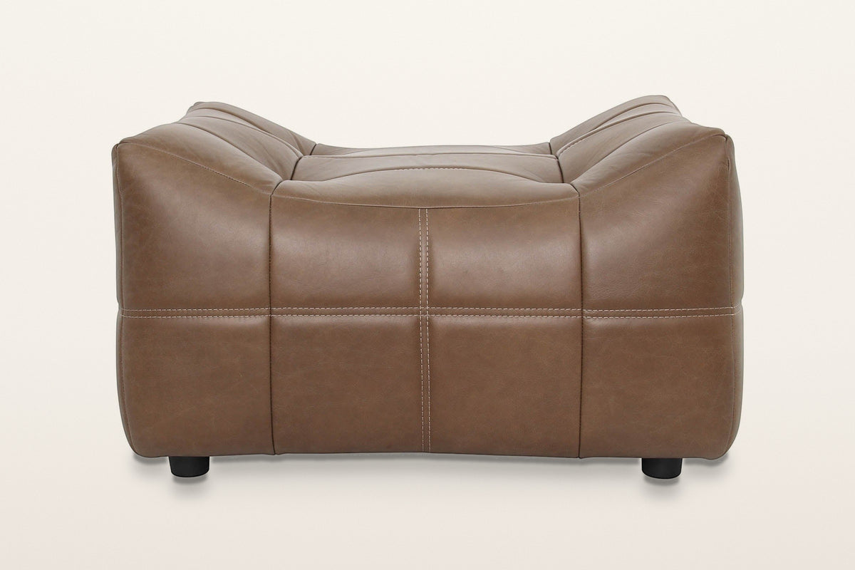 Sassocorvaro ottoman in Antique Sienna from the dipped side on a warm white studio backdrop: the top curves down in a shallow