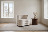 Sauze accent chair in beige velvet on a light grey rug in a limewashed stone living room in Quebec City's Old Town, old stone houses through the deep window