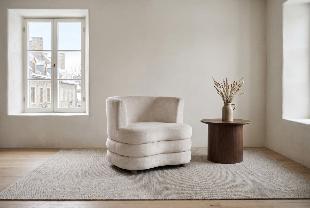 Sauze accent chair in beige velvet on a light grey rug in a limewashed stone living room in Quebec City's Old Town, old stone houses through the deep window