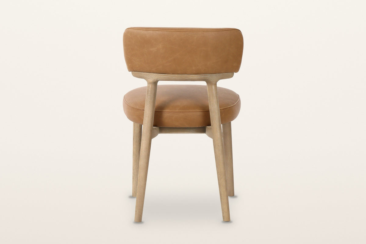 The back of the Savoca dining chair in Tawny leather on a warm white studio backdrop: the back band
