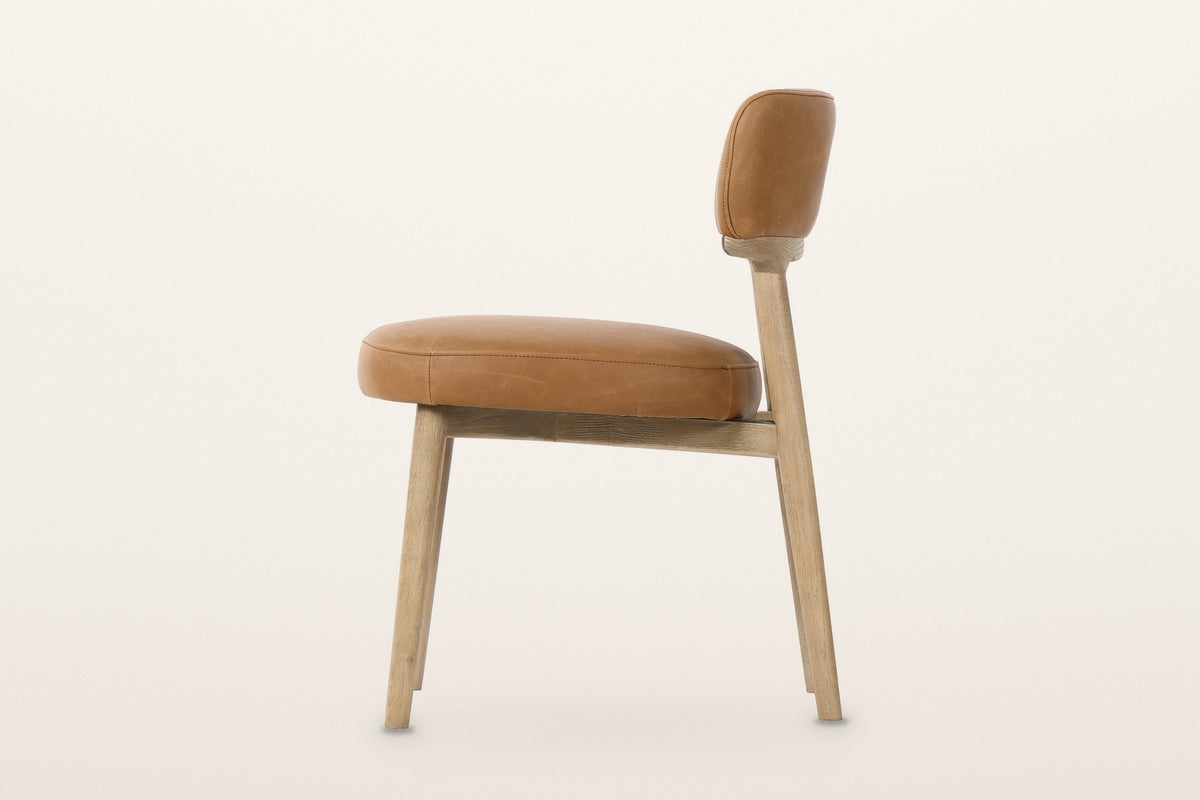Savoca dining chair in Tawny leather, side view on a warm white studio backdrop: the rear leg runs up into the back post unde