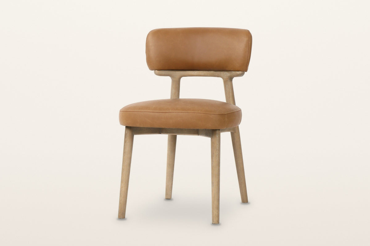 Savoca dining chair in Tawny leather, three-quarter view on a warm white studio backdrop: a padded back band on a curved ash
