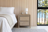 Front view of the Scheggino nightstand in pale reclaimed pine beside the bed in a Parksville beach house bedroom